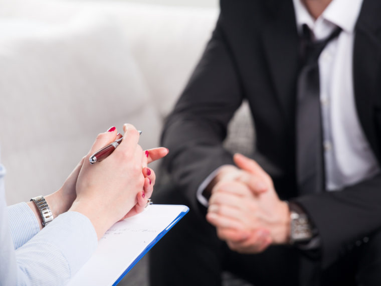 Over the shoulder view, of a business man sit on a couch talking to his psychiatrist